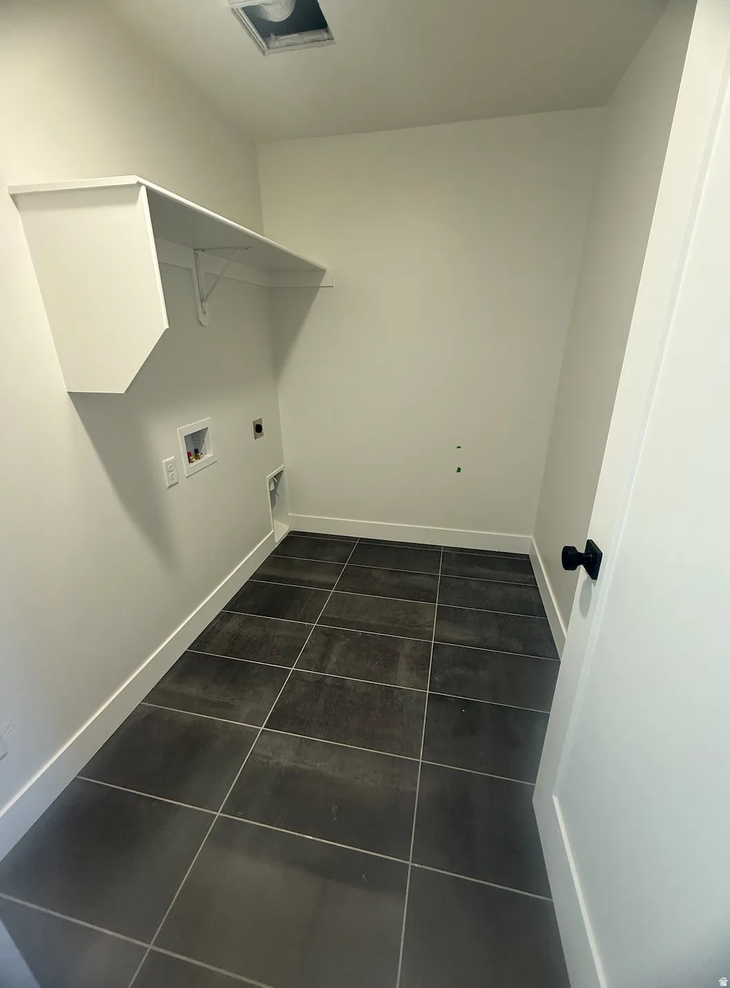 Utility room featuring dark gray tile flooring, white baseboards, and a white built-in shelf