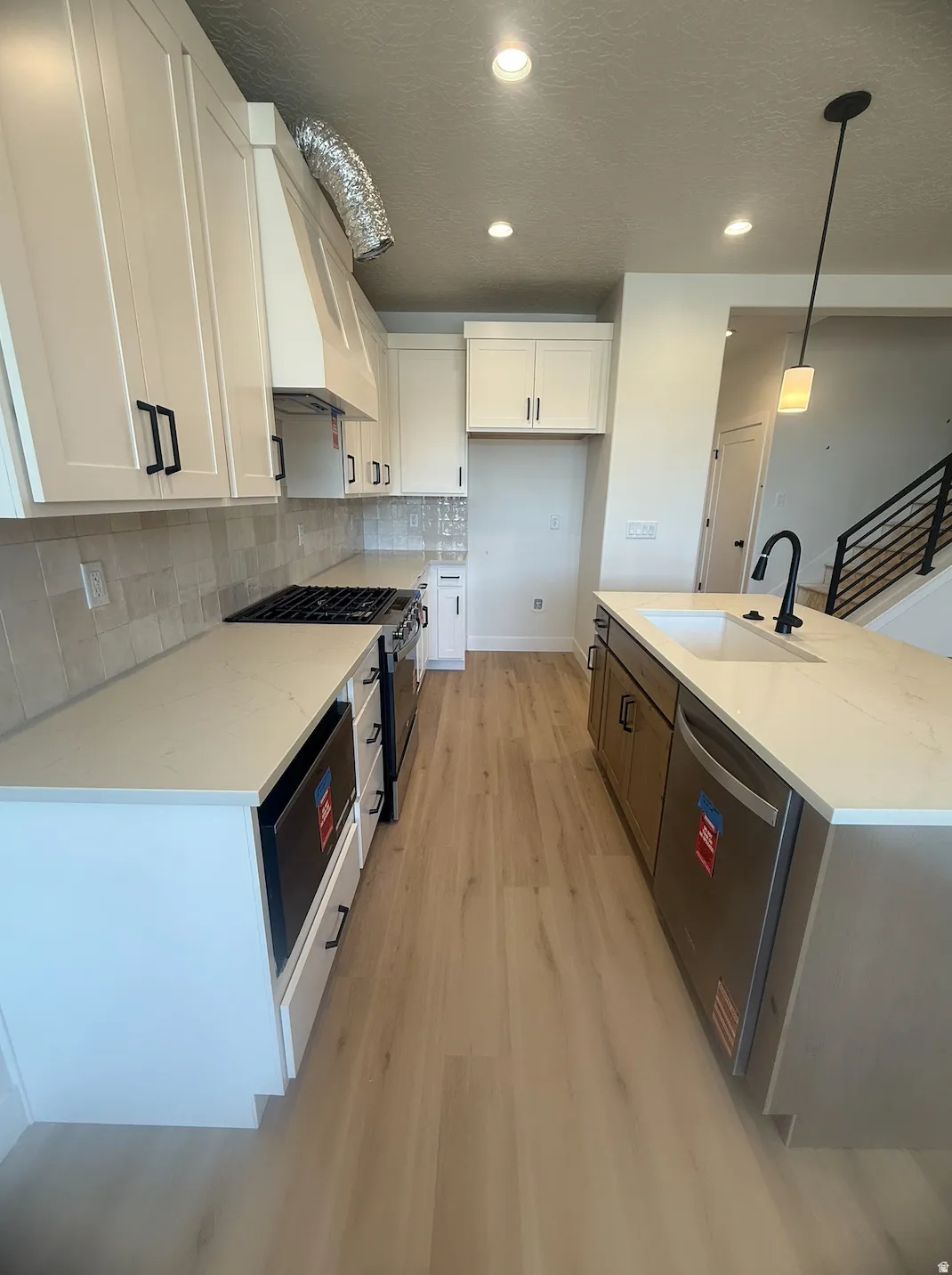 Open-concept kitchen featuring light-toned wood-finish flooring, white cabinetry with black hardware, light-colored countertops, and a full tile backsplash