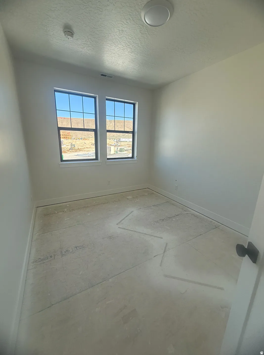 Room featuring two large windows with black frames, white walls, and a flat ceiling light fixture