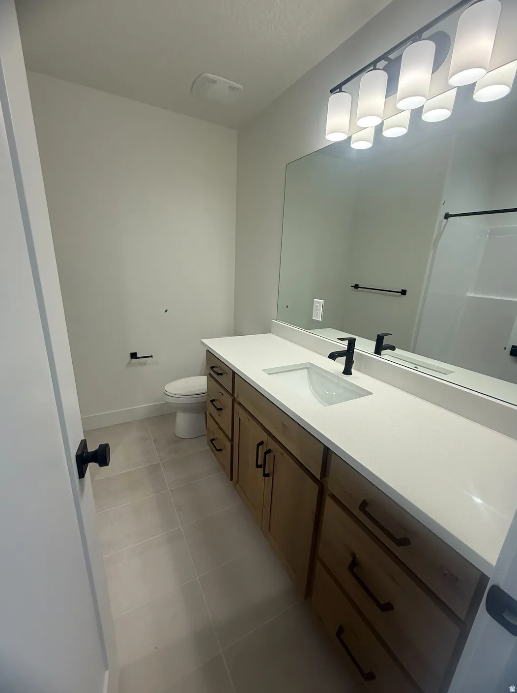 Full bathroom featuring a wood-finish vanity with ample storage, a white countertop, an undermount sink with a matte black faucet, and a large wall-mounted mirror