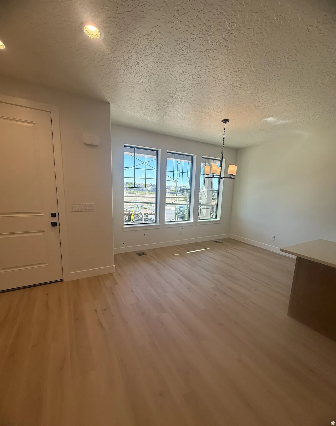Open-concept living area featuring wood-finish flooring, a contemporary chandelier, recessed lighting, and a series of three tall windows