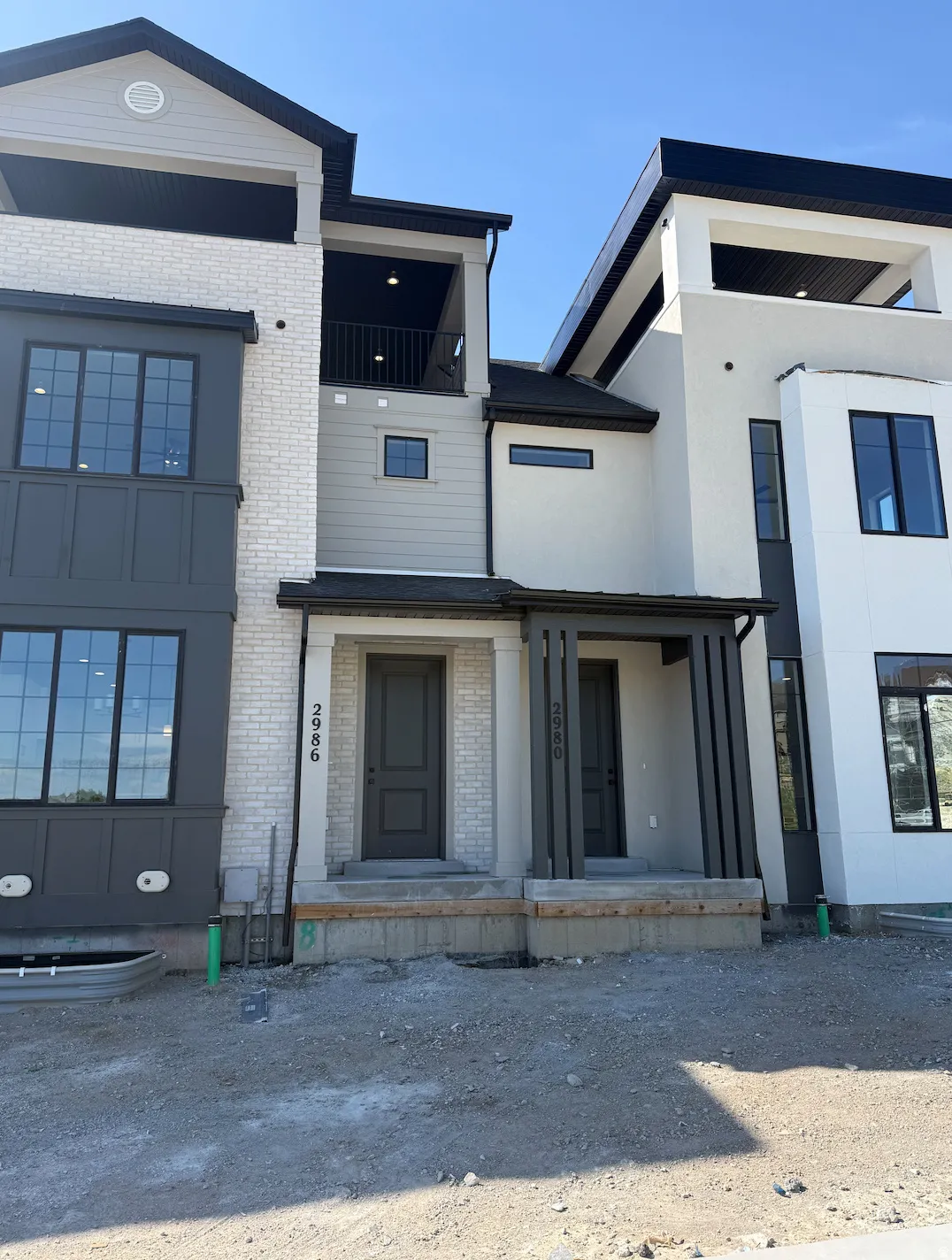 Contemporary townhouse exterior featuring a white brick facade, dark gray siding, and black-framed windows