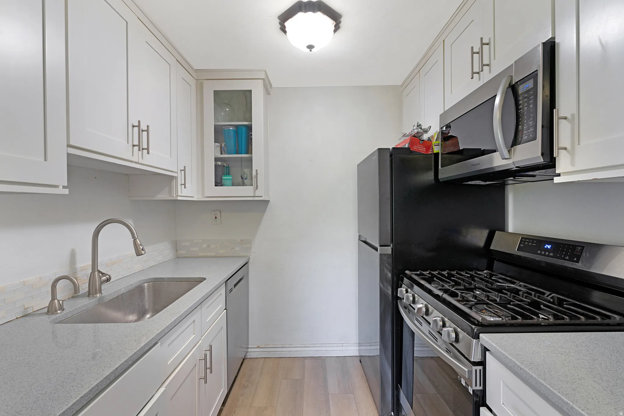 Compact kitchen featuring light gray countertops and white shaker cabinetry with brushed nickel hardware