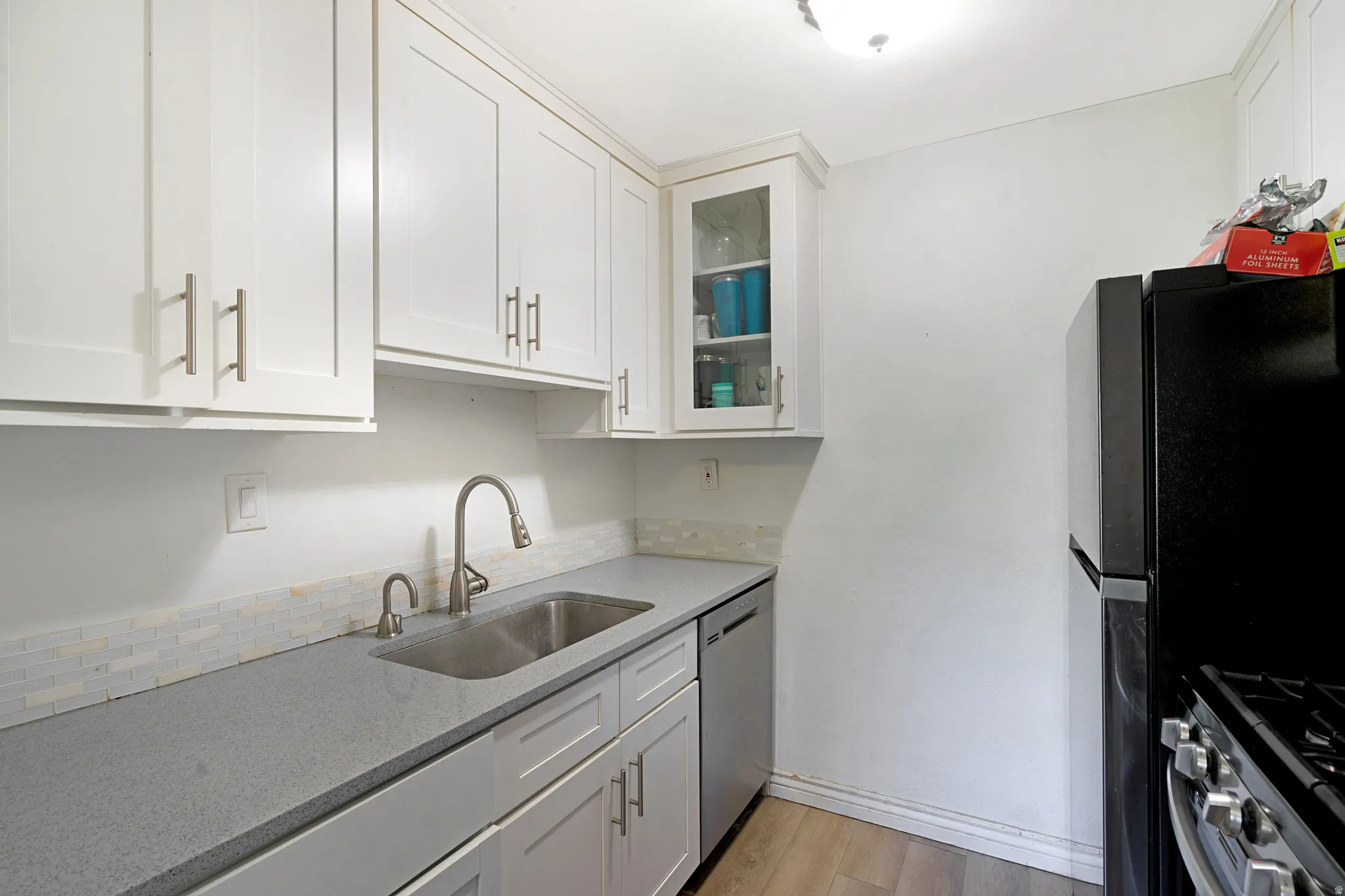 Kitchen featuring white shaker-style cabinetry, a stainless steel sink with a high-arc faucet, and gray countertops