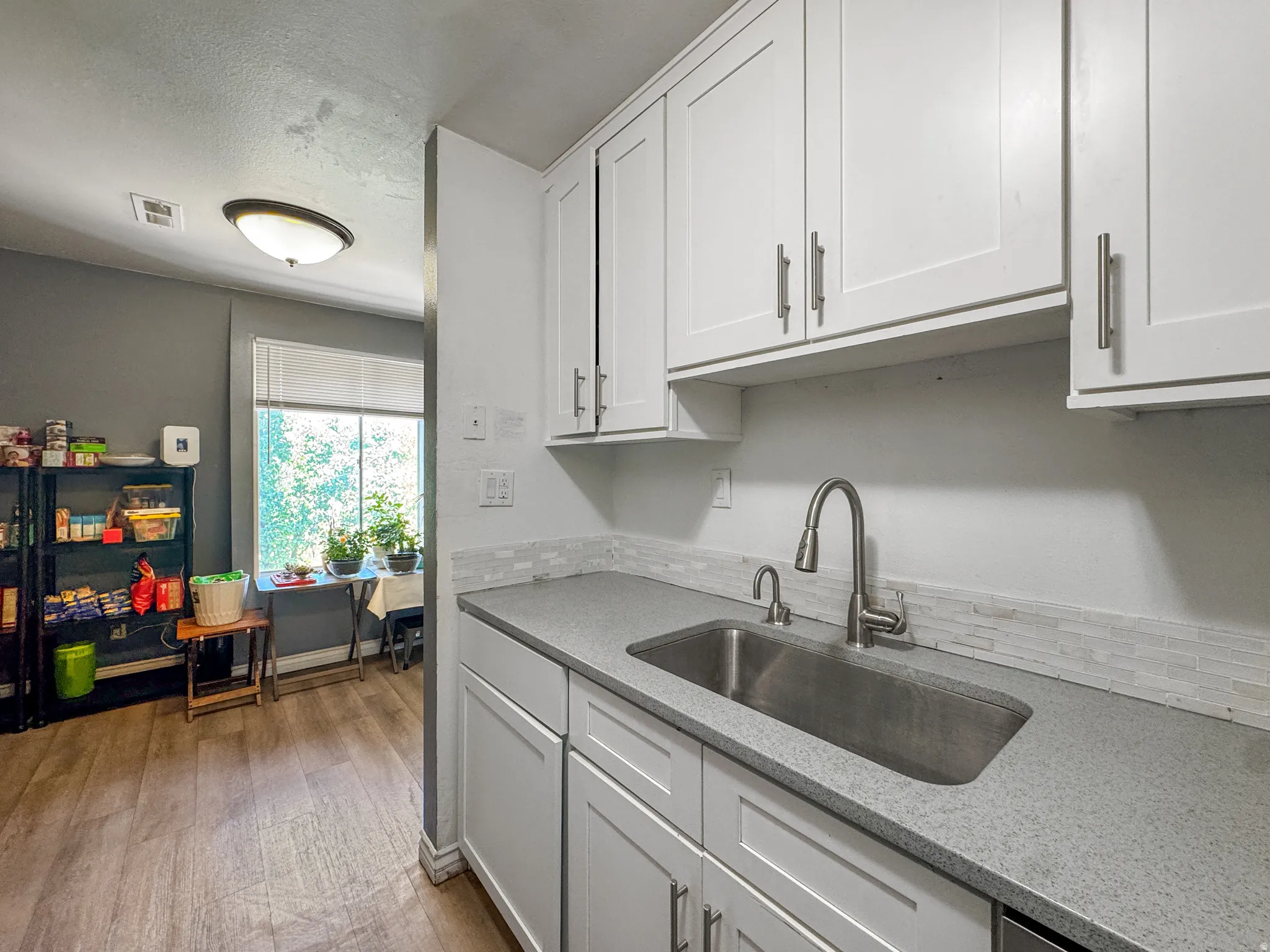 Contemporary kitchen featuring white shaker cabinetry, stainless steel sink, speckled gray countertop, and a white tile backsplash
