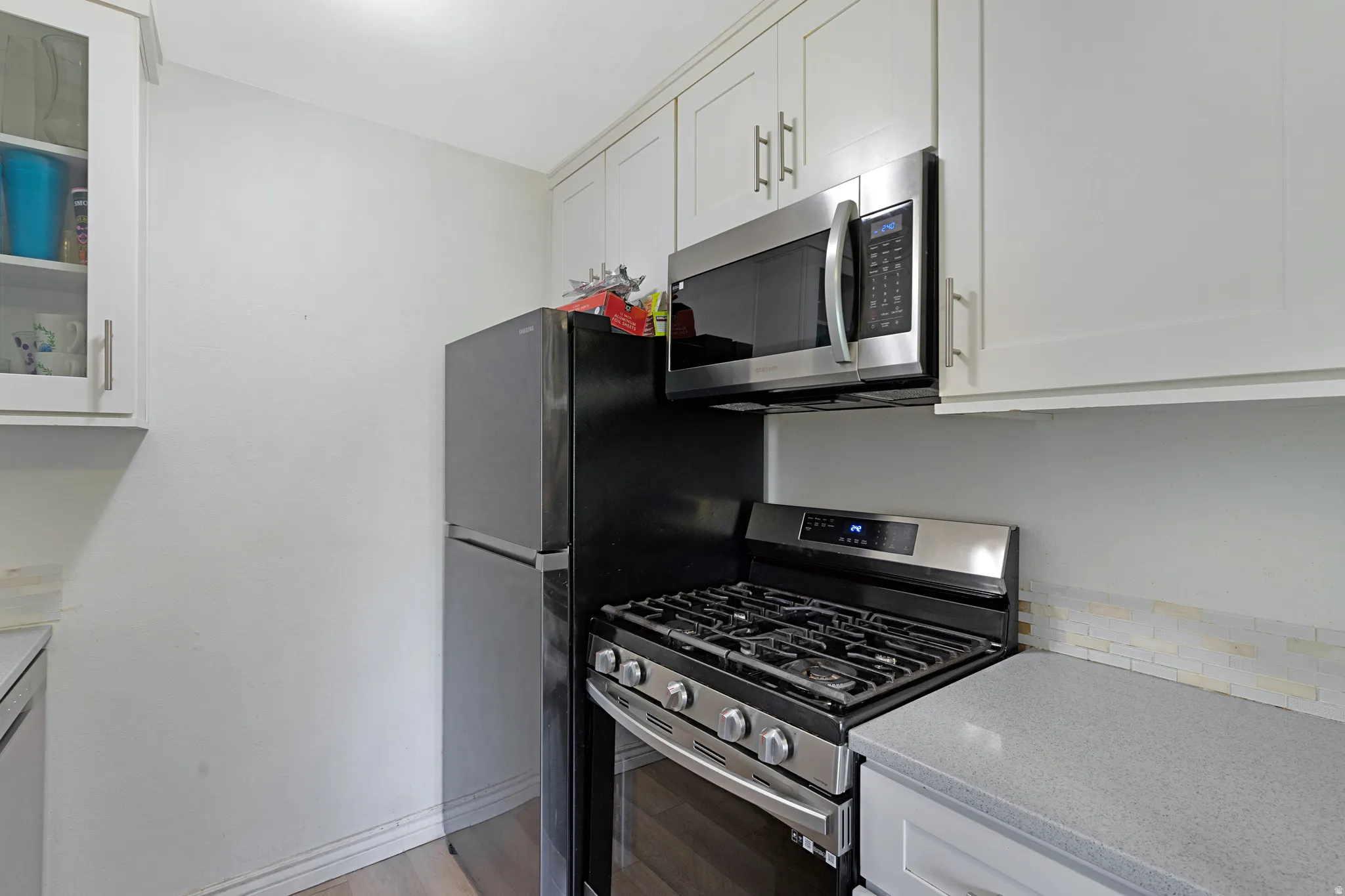 Kitchen featuring light cabinetry, stainless steel microwave, gas range, black refrigerator, and light gray countertops with a mosaic tile backsplash