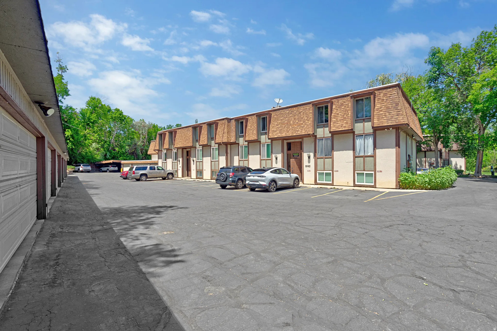 Multi-unit building exterior featuring a brown gambrel roofline, light-colored siding, and individual entrances