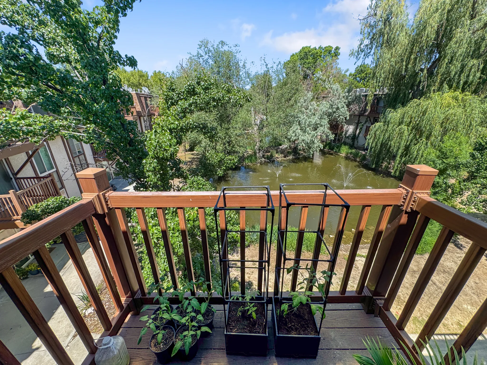 Exterior balcony with wood-finish decking and railing overlooking a pond with water features