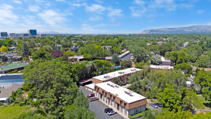 Aerial perspective showcasing multiple townhouse buildings with pitched roofs, surrounding lush green trees and a paved parking area