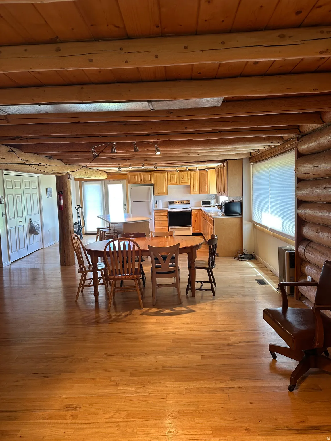 Open-concept living area with wood-finish flooring, exposed log beam ceiling, and log wall accents