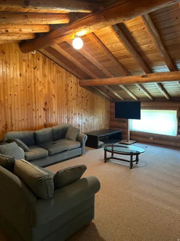Carpeted living space featuring wood paneling and exposed wood beams