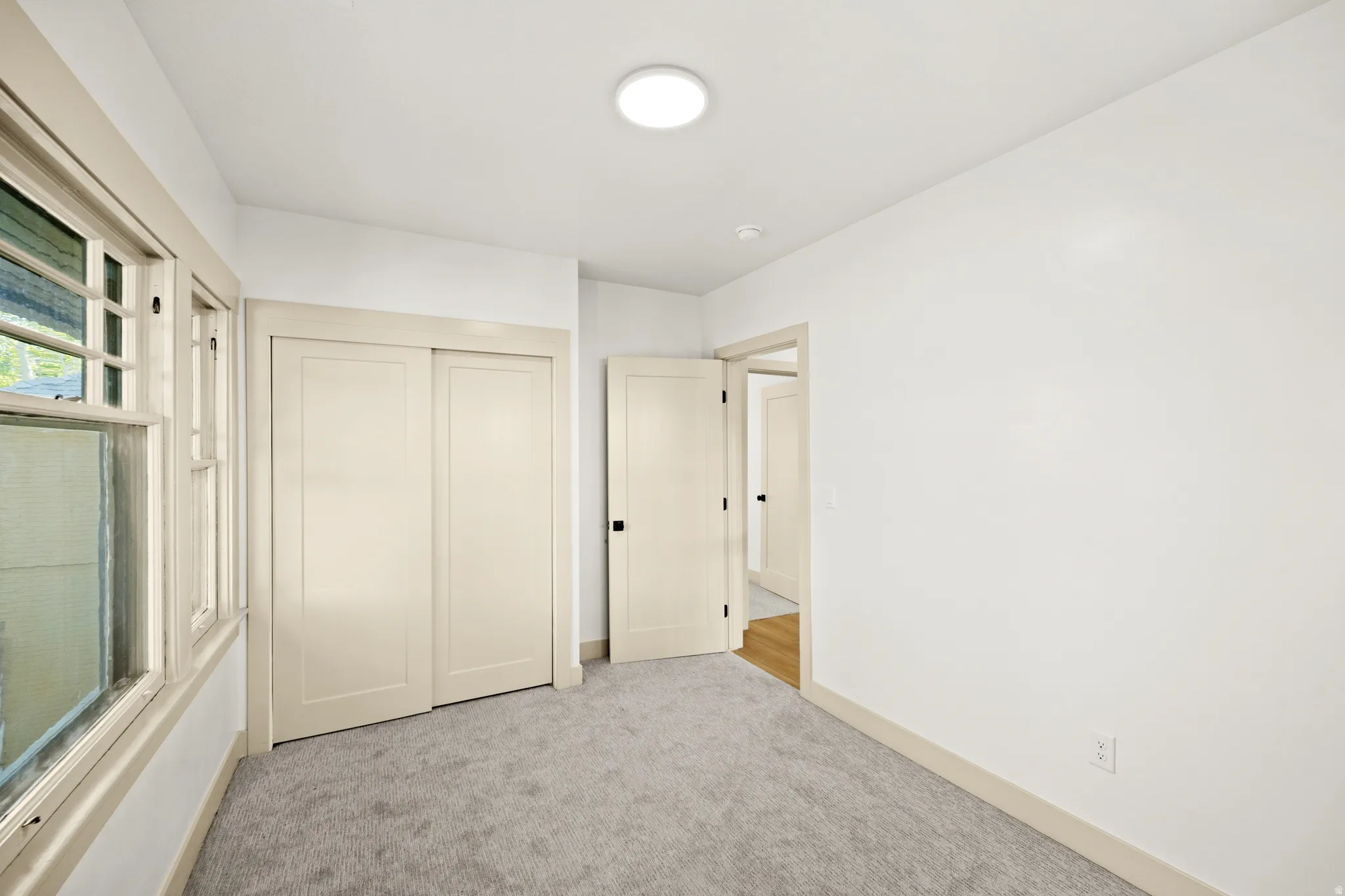 Carpeted room featuring white walls, a single ceiling light fixture, a window with mullions, and two light-colored doors with black hardware