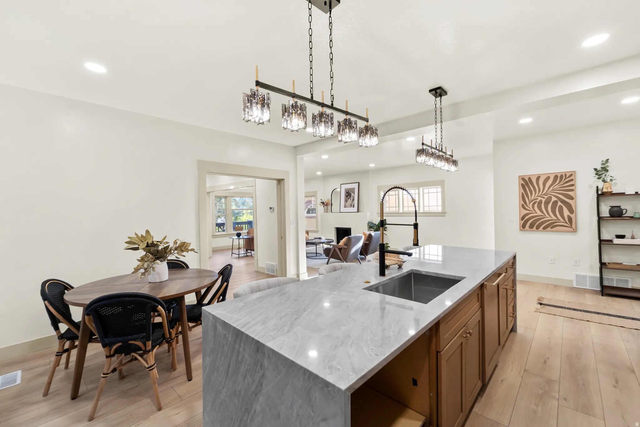Spacious kitchen featuring a large waterfall island with integrated sink, wood-finish flooring, recessed lighting, and contemporary pendant light fixtures
