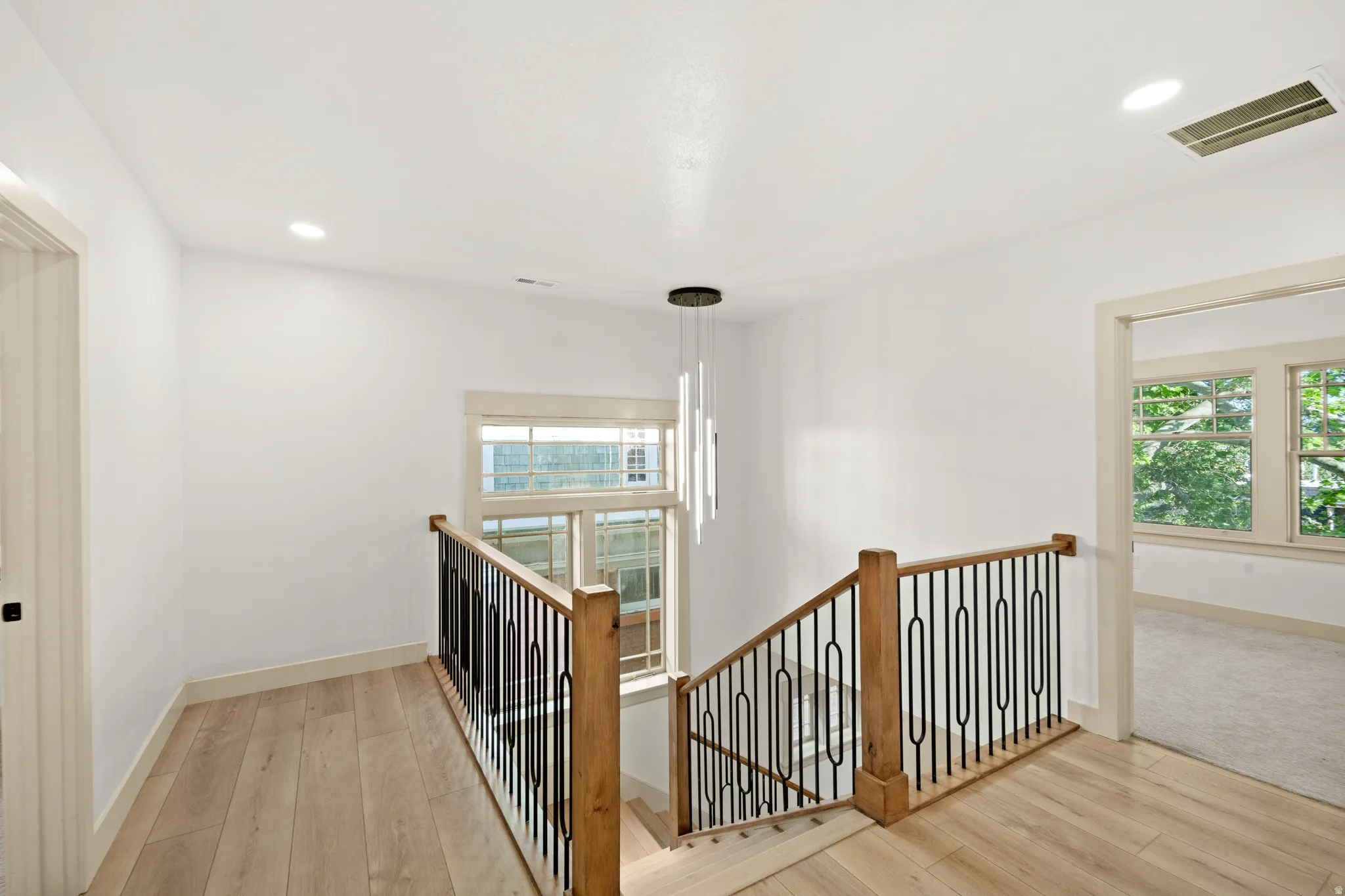 Upper-level landing featuring light wood-finish flooring, a contemporary linear pendant light, and recessed ceiling lighting