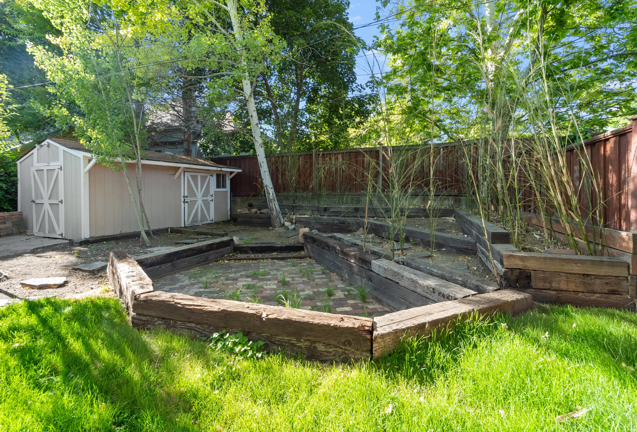 Expansive backyard featuring a manicured lawn, a detached storage shed with double doors, and tiered raised garden beds crafted from wood timbers