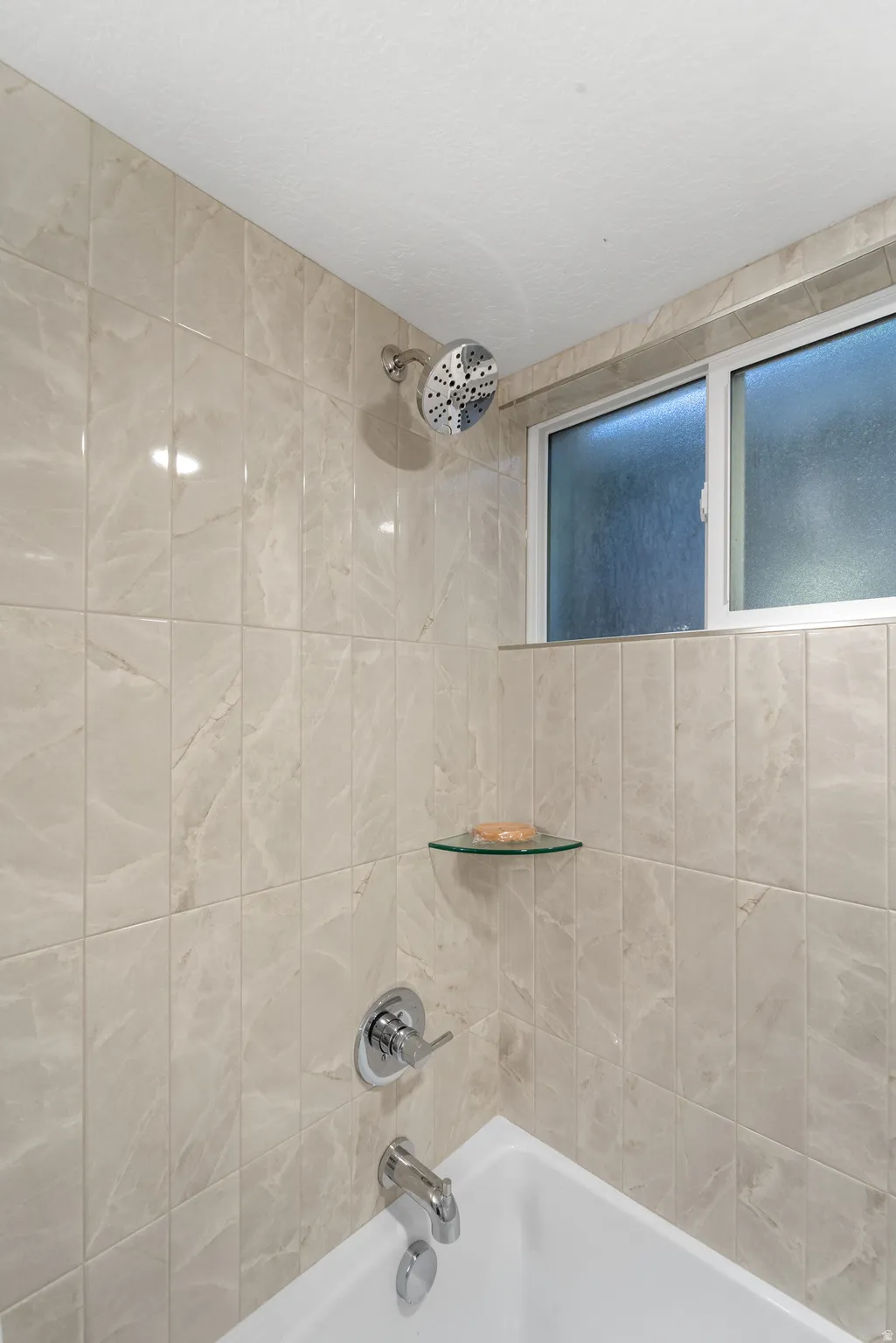 Bathtub and shower combination featuring neutral-toned tile surround, chrome fixtures, and a privacy window