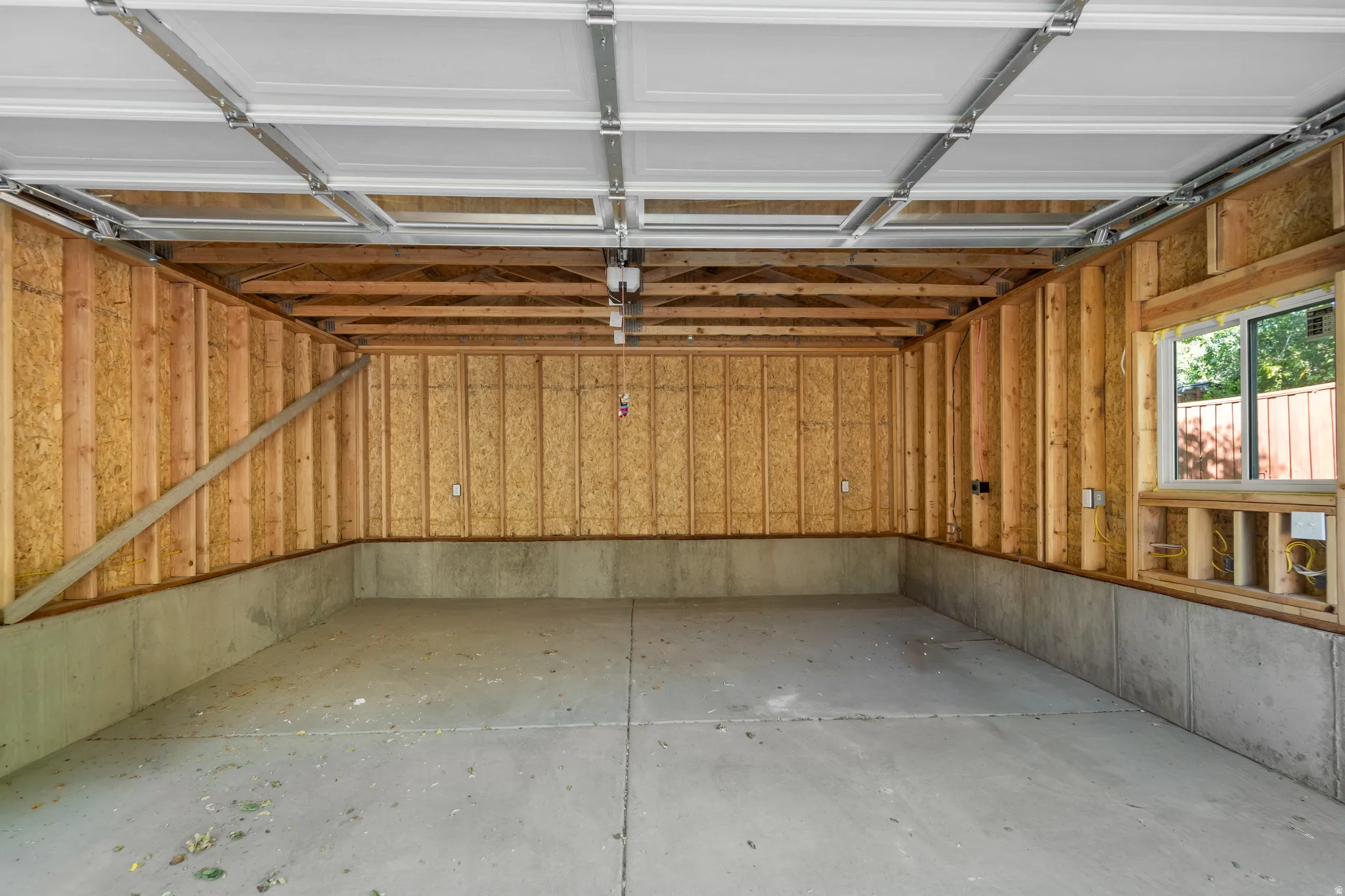 Unfinished garage interior featuring concrete flooring, exposed wood framing, and a white garage door with track system