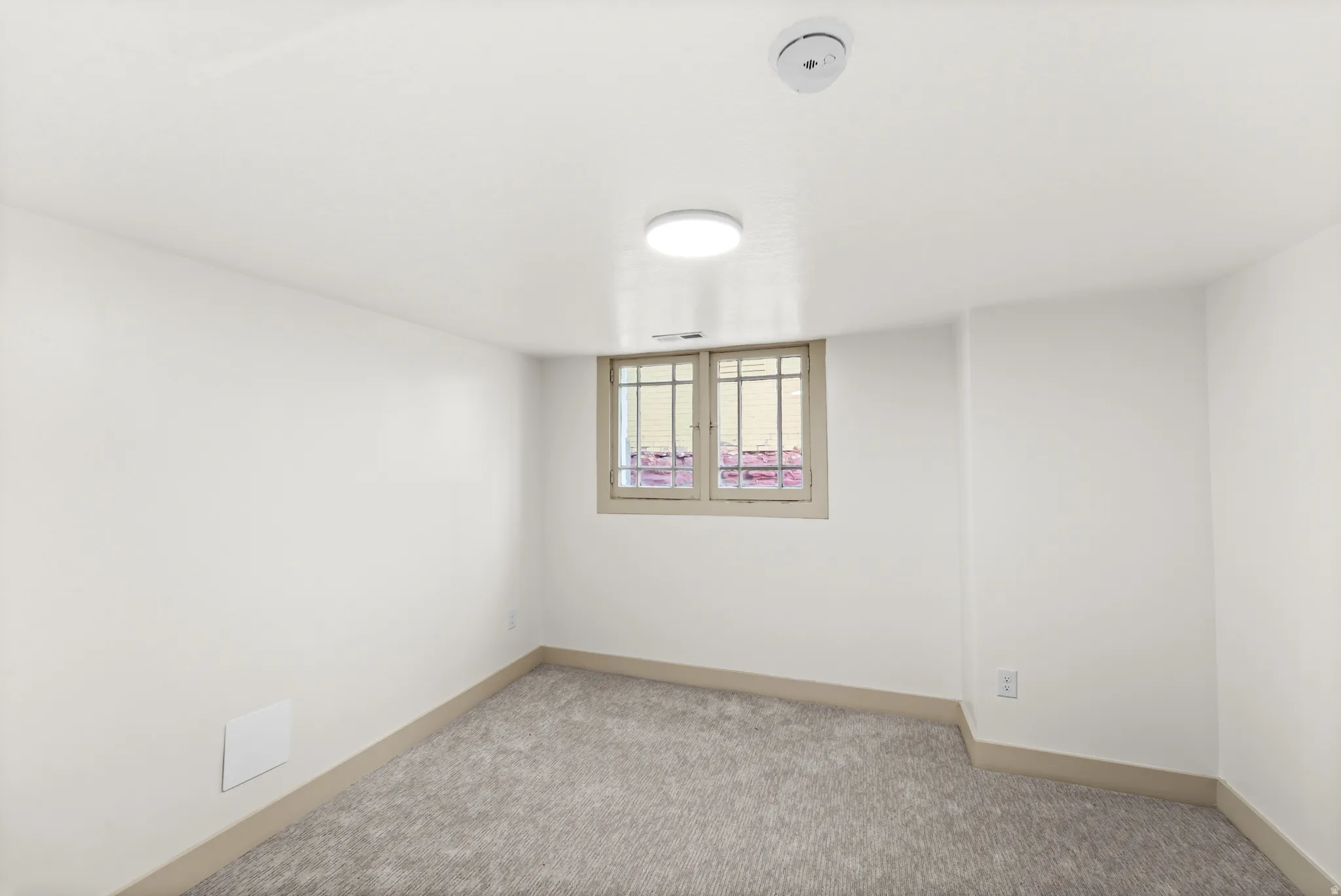 Carpeted room featuring a window with security bars, white walls, light gray baseboards, and ceiling-mounted lighting