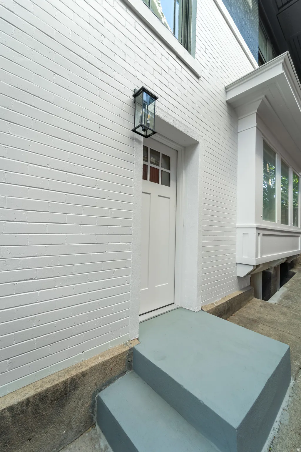 White painted brick exterior with a transom window entry, featuring a black framed outdoor wall lantern