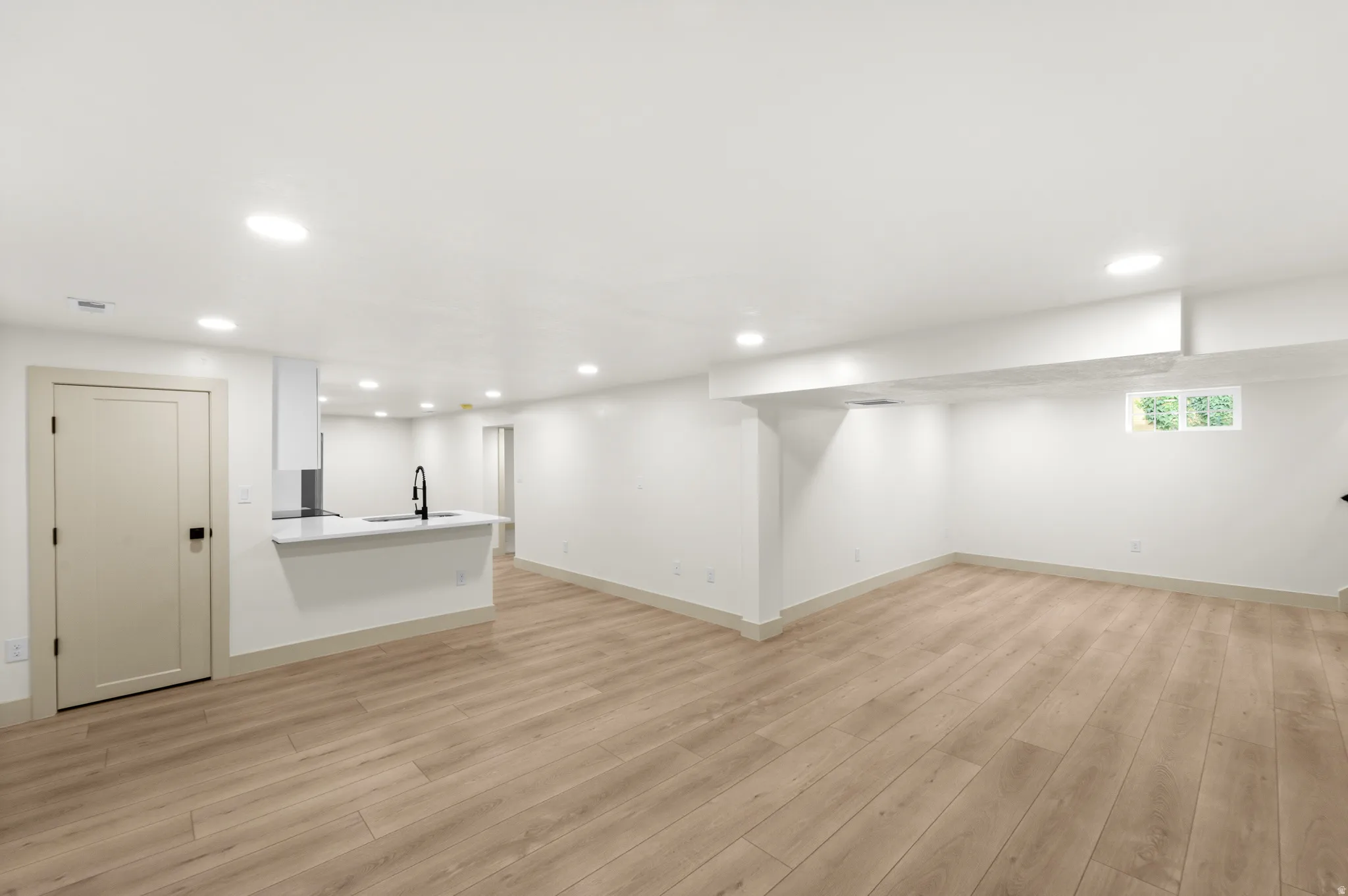 Expansive open-concept room featuring wood-finish flooring, recessed lighting, and a contemporary kitchen island with a sink and matte black faucet