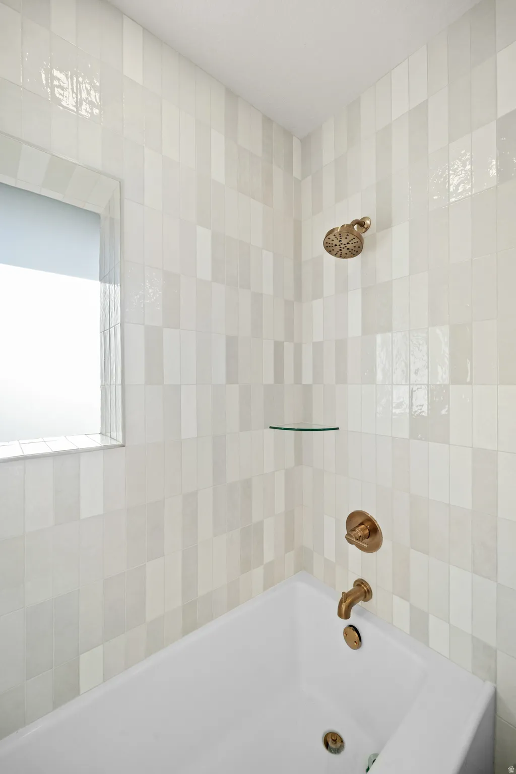 Bathtub and shower combination featuring a white soaking tub, multi-toned vertical tile surround, and bronze fixtures