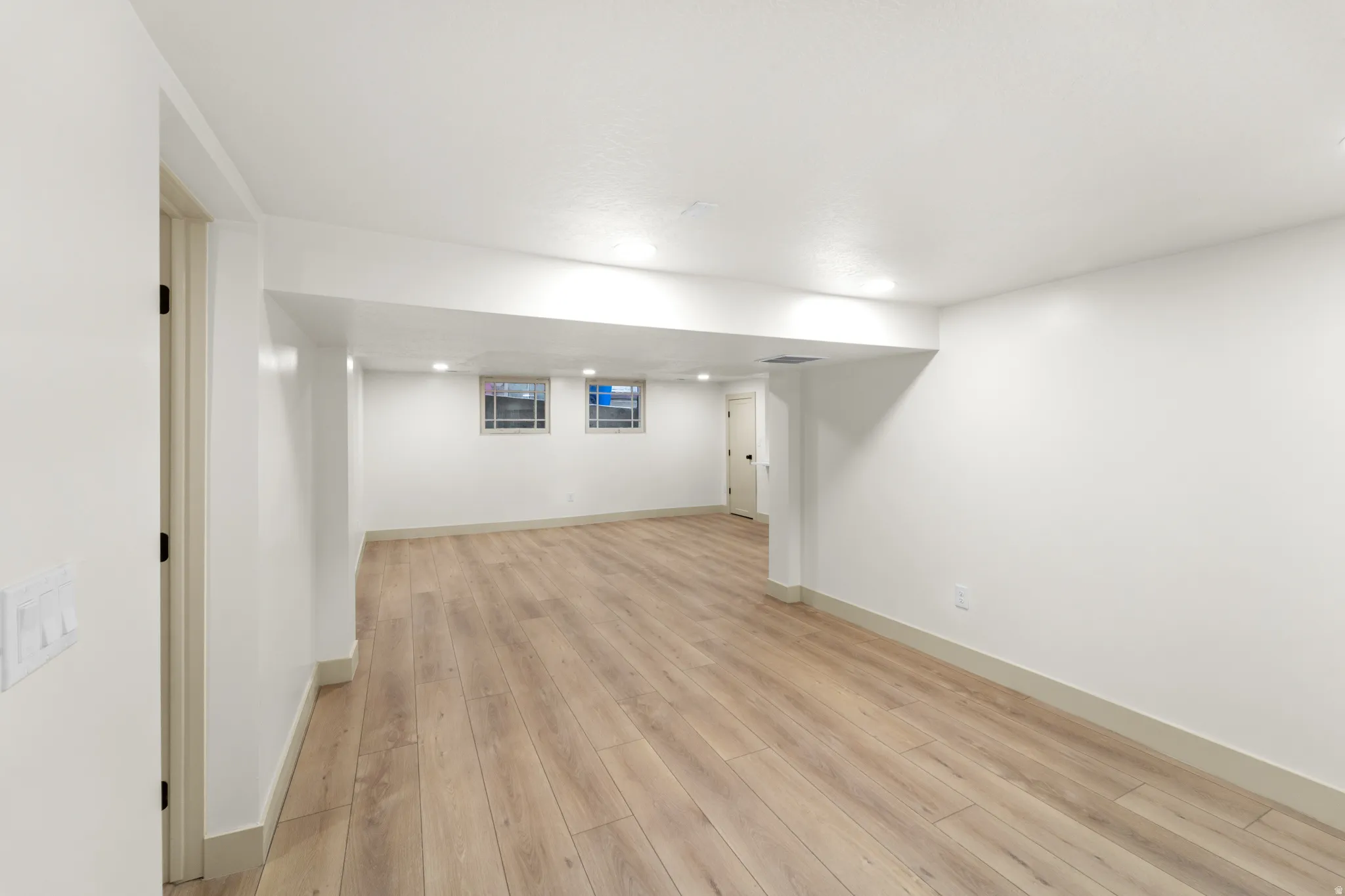 Open space featuring wood-finish flooring, white painted walls, recessed lighting, and two small windows