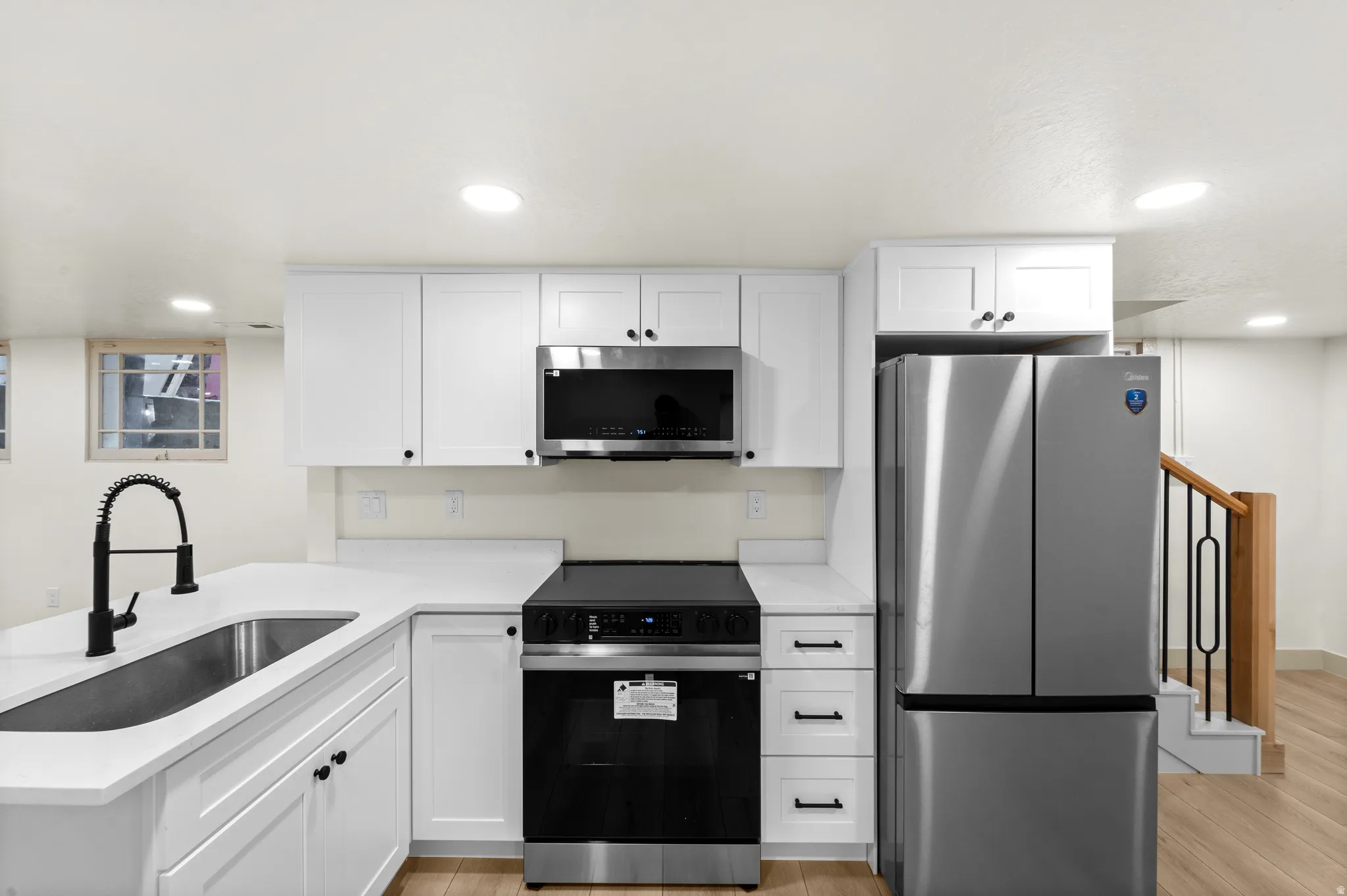 Kitchen featuring white shaker cabinetry, stainless steel appliances, quartz countertops, a matte black gooseneck faucet, and wood-finish flooring