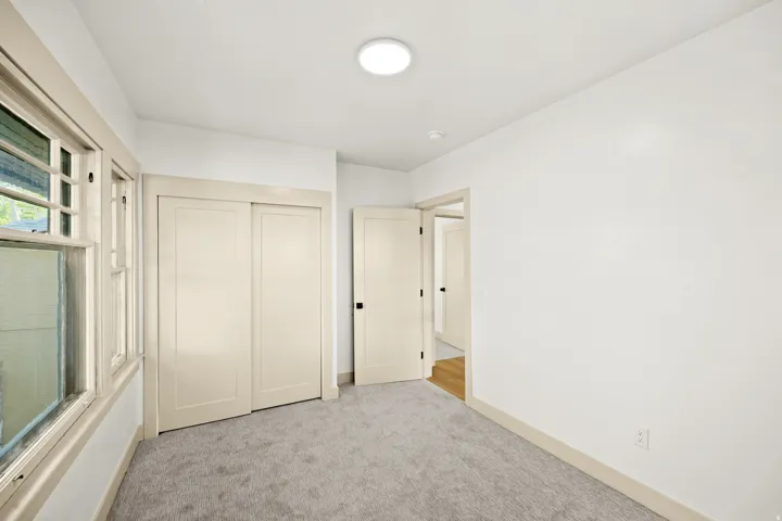 Carpeted room featuring white walls, a single ceiling light fixture, a window with mullions, and two light-colored doors with black hardware