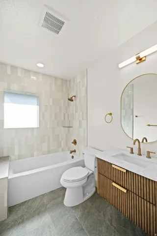 Modern bathroom featuring a soaking tub with patterned tile surround, a sleek toilet, and a floating vanity with a fluted wood-finish facade and marble-finish countertop