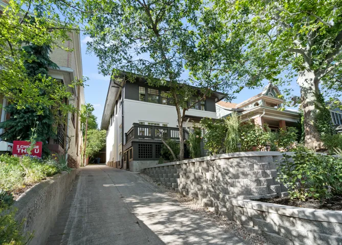 Modern exterior featuring a white facade with dark trim accents, a balcony with dark railings, and a concrete driveway
