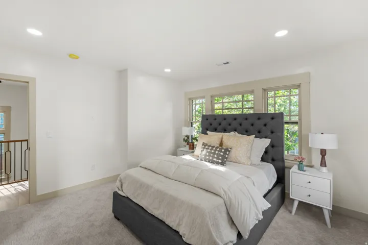 Carpeted bedroom featuring a tufted headboard, multiple windows with wood trim, recessed lighting, and a neutral color palette