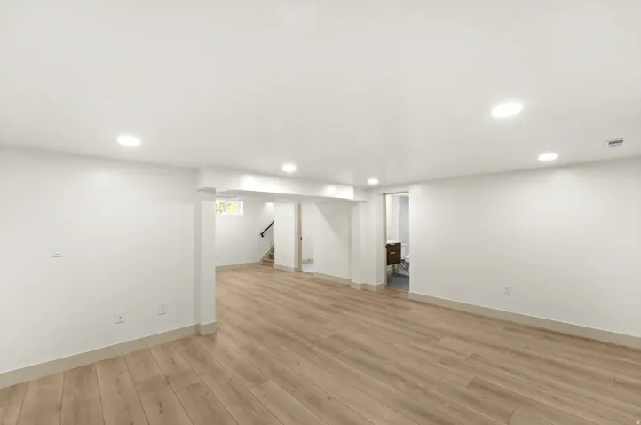 Expansive room featuring wood-finish flooring, recessed lighting, white walls, and a visible staircase