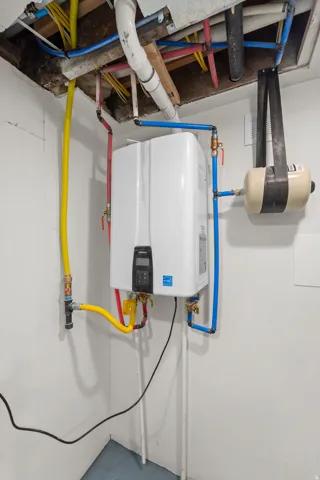 Tankless water heater installation featuring exposed plumbing and wiring