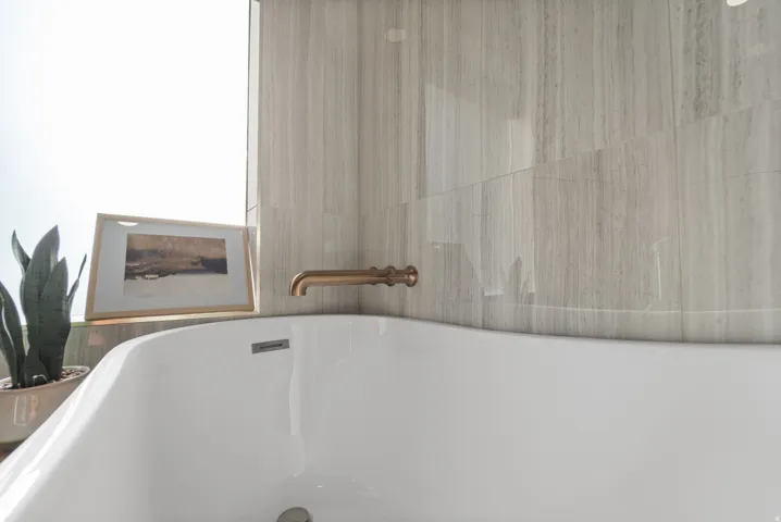 Freestanding white soaking tub featuring a wall-mounted bronze-finish faucet