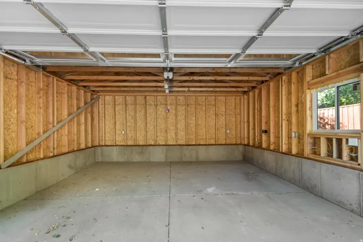 Unfinished garage interior featuring concrete flooring, exposed wood framing, and a white garage door with track system