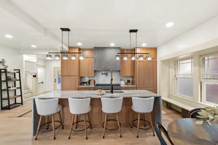 Gourmet kitchen featuring a large island with seating, pendant lighting, professional-grade range, full-height cabinetry, and wood-finish flooring