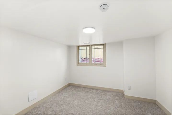 Carpeted room featuring a window with security bars, white walls, light gray baseboards, and ceiling-mounted lighting