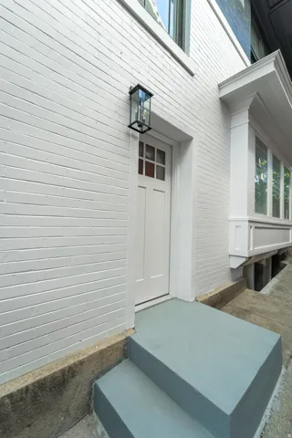 White painted brick exterior with a transom window entry, featuring a black framed outdoor wall lantern