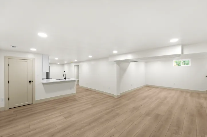 Expansive open-concept room featuring wood-finish flooring, recessed lighting, and a contemporary kitchen island with a sink and matte black faucet