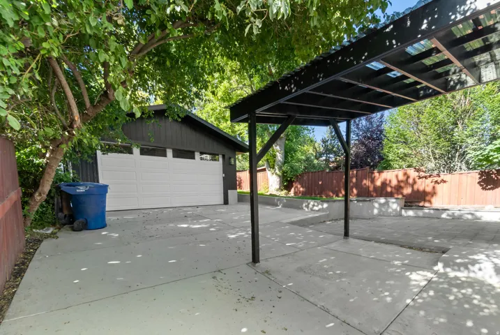 Paved concrete driveway and parking area featuring a black metal pergola