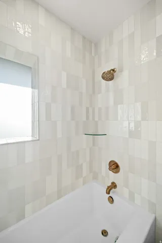 Bathtub and shower combination featuring a white soaking tub, multi-toned vertical tile surround, and bronze fixtures