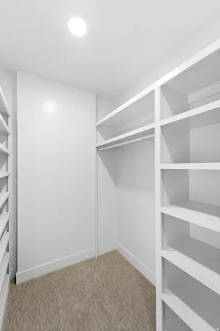 Walk-in closet featuring built-in shelving, hanging rod, recessed lighting, and carpet flooring