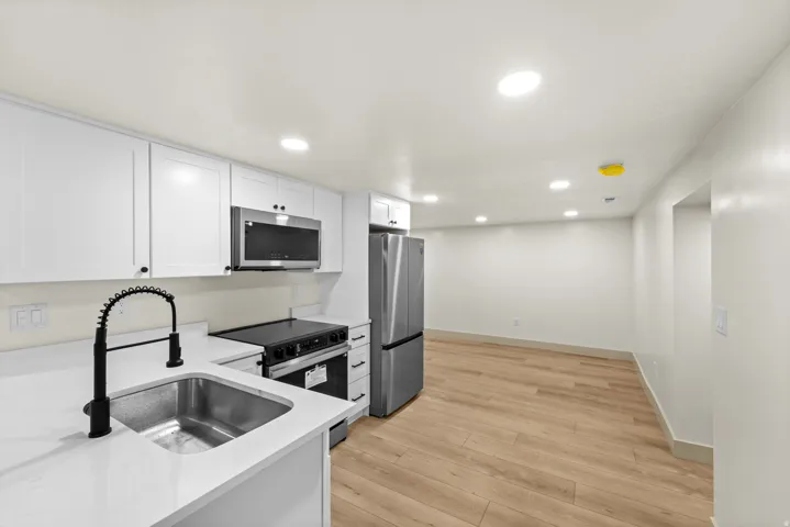 Kitchen featuring white cabinetry, a stainless steel sink with a matte black pull-down faucet, white countertops, and stainless steel appliances including a microwave, range, and refrigerator