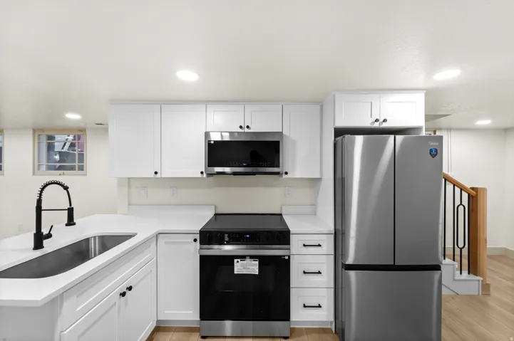 Kitchen featuring white shaker cabinetry, stainless steel appliances, quartz countertops, a matte black gooseneck faucet, and wood-finish flooring