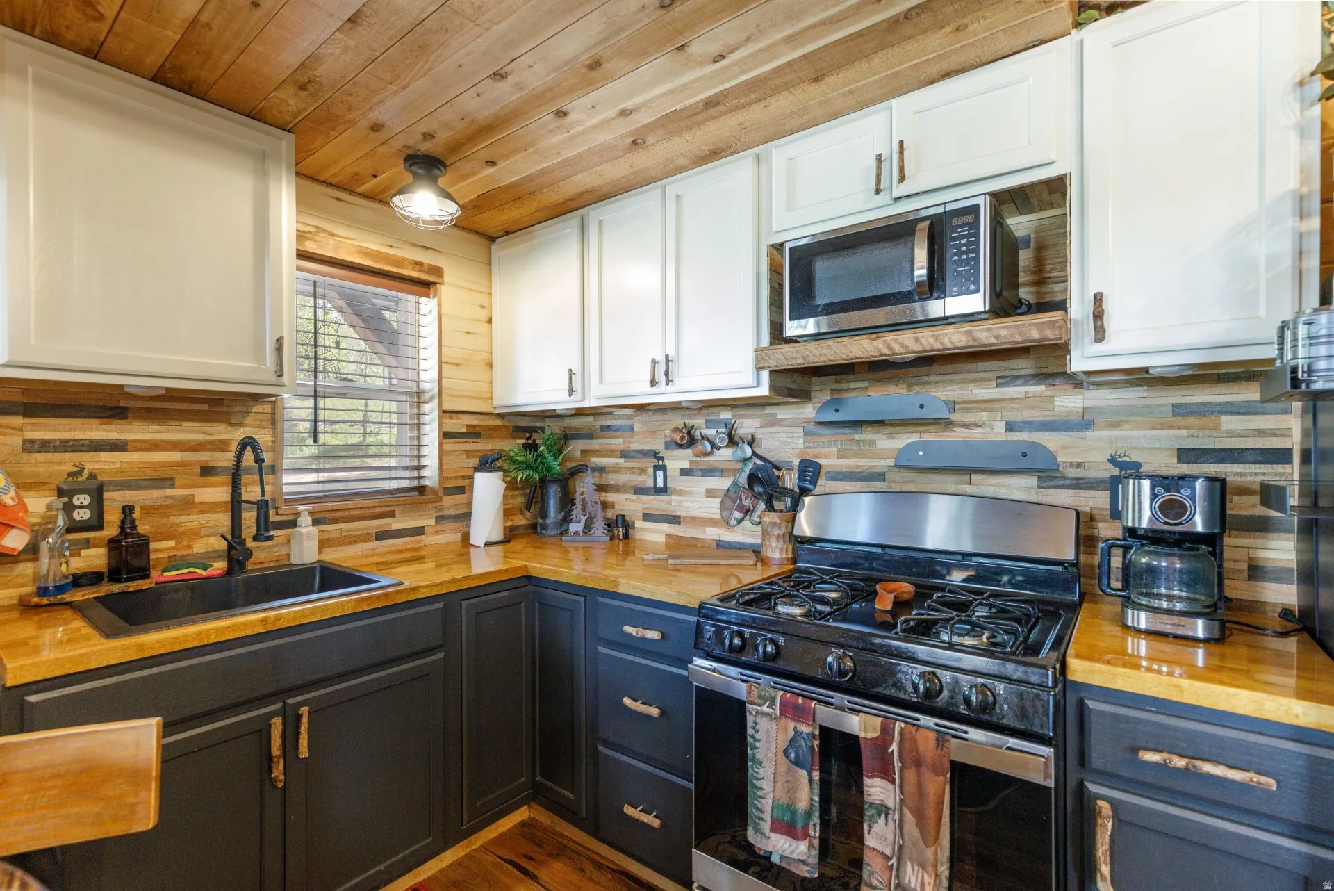 Kitchen featuring wood-finish ceiling, wood-finish countertops, two-tone cabinetry, stainless steel range, and a mosaic tile backsplash