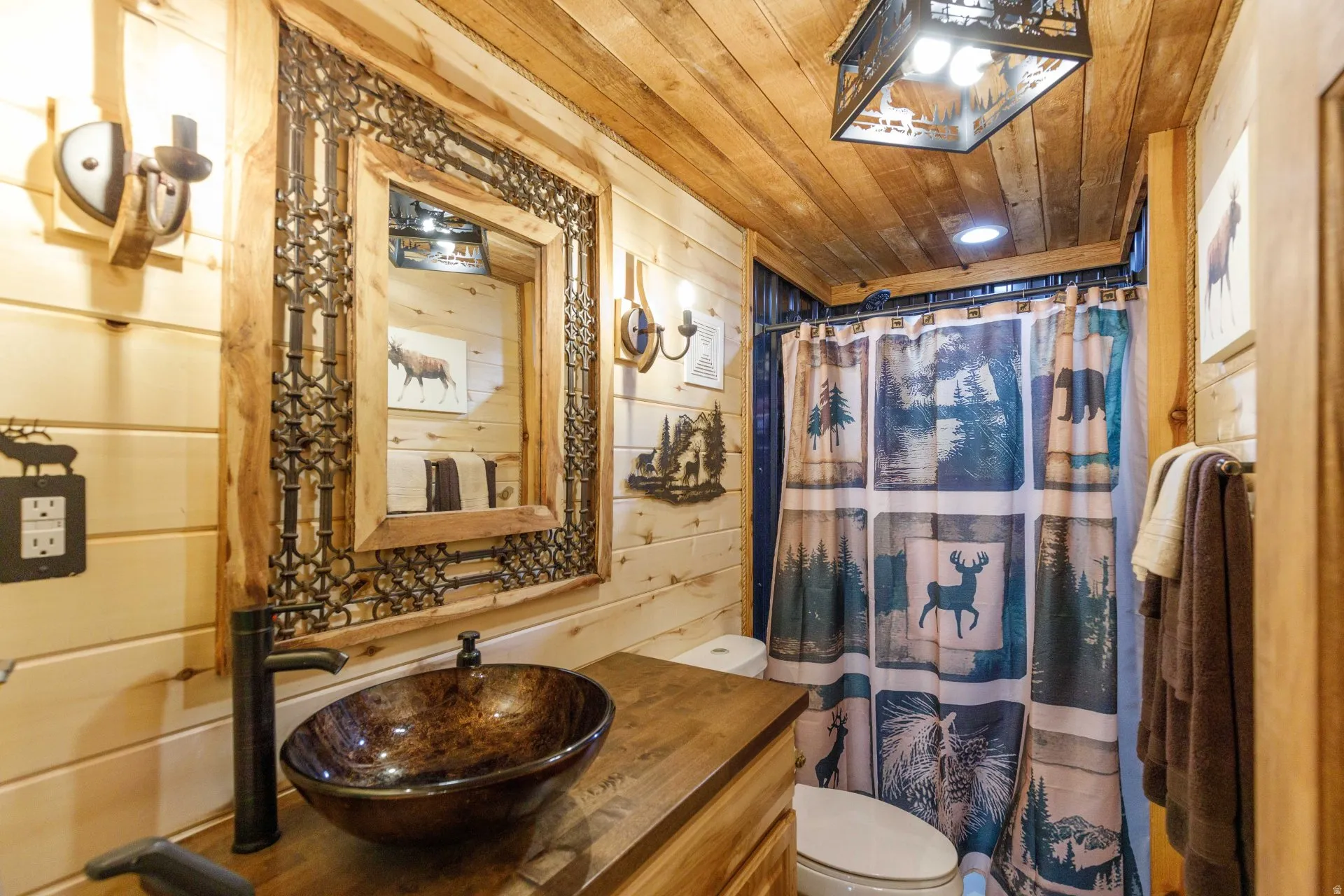 Bathroom featuring wood-finish walls and ceiling, a rectangular mirror with an ornate metal frame, a bowl-style vessel sink, and an oil-rubbed bronze faucet