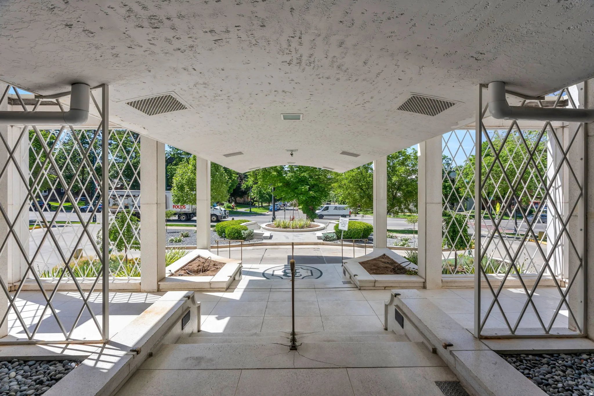 Covered outdoor entrance featuring a textured ceiling, geometric lattice work, integrated planters, and a central circular motif on the ground