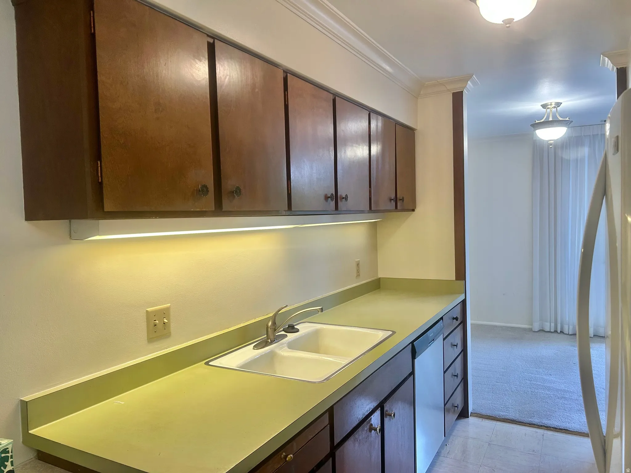 Kitchen featuring wood cabinetry, a dual basin sink, integrated dishwasher, under-cabinet lighting, and a light-colored countertop