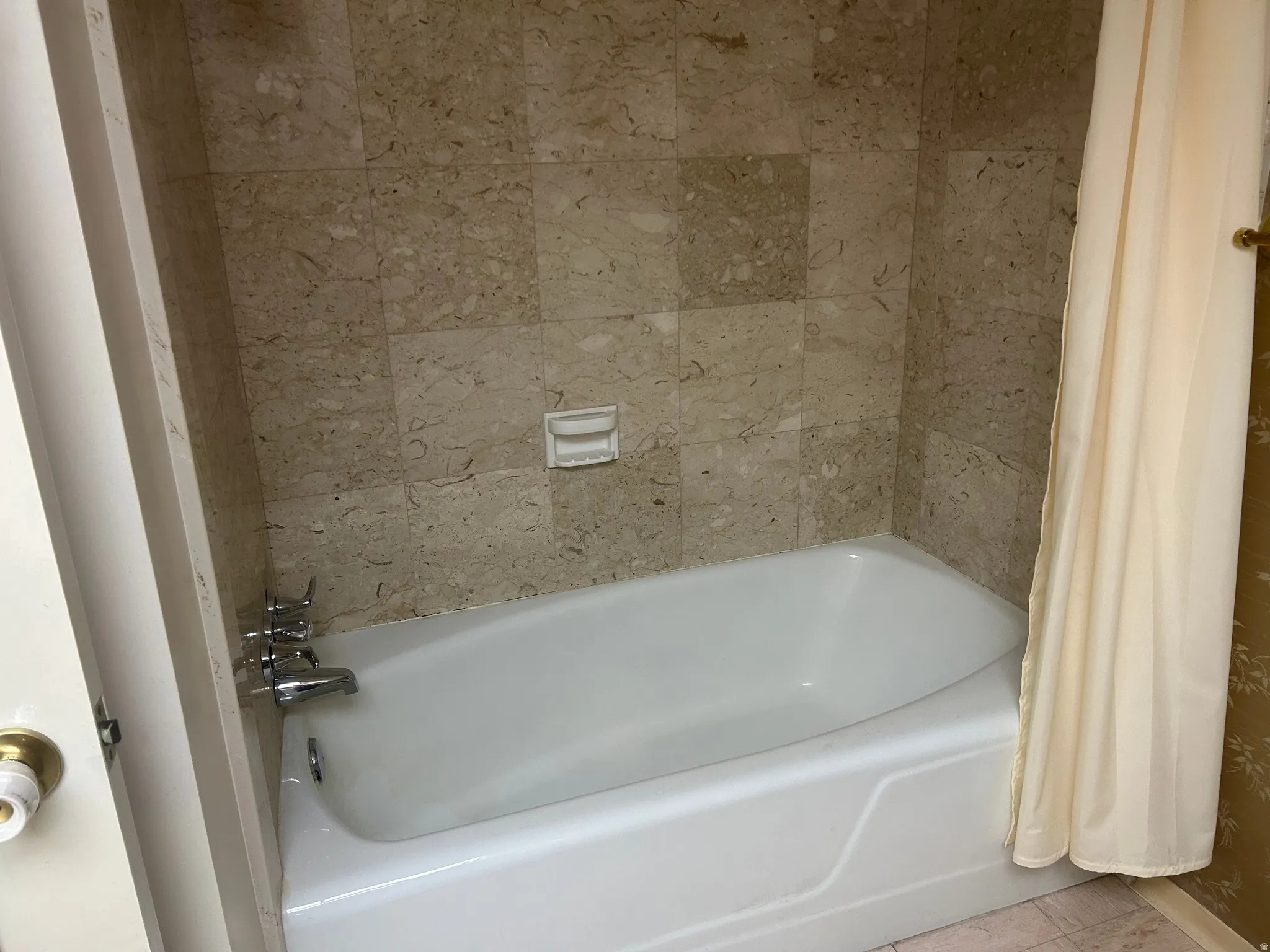 Bathtub with chrome fixtures, surrounded by light-toned, textured wall tiles