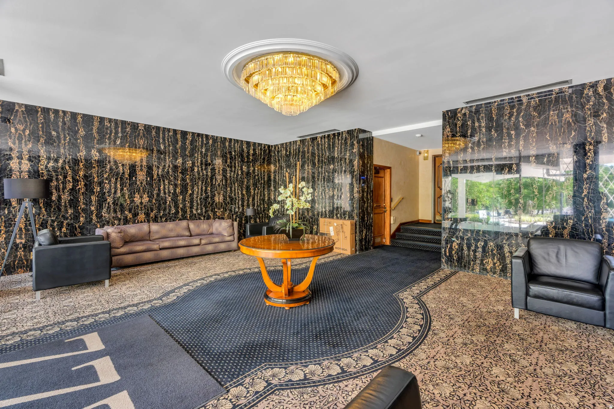 Lobby featuring a large crystal chandelier, patterned carpeting, black and gold wall paneling, and a polished wood central table